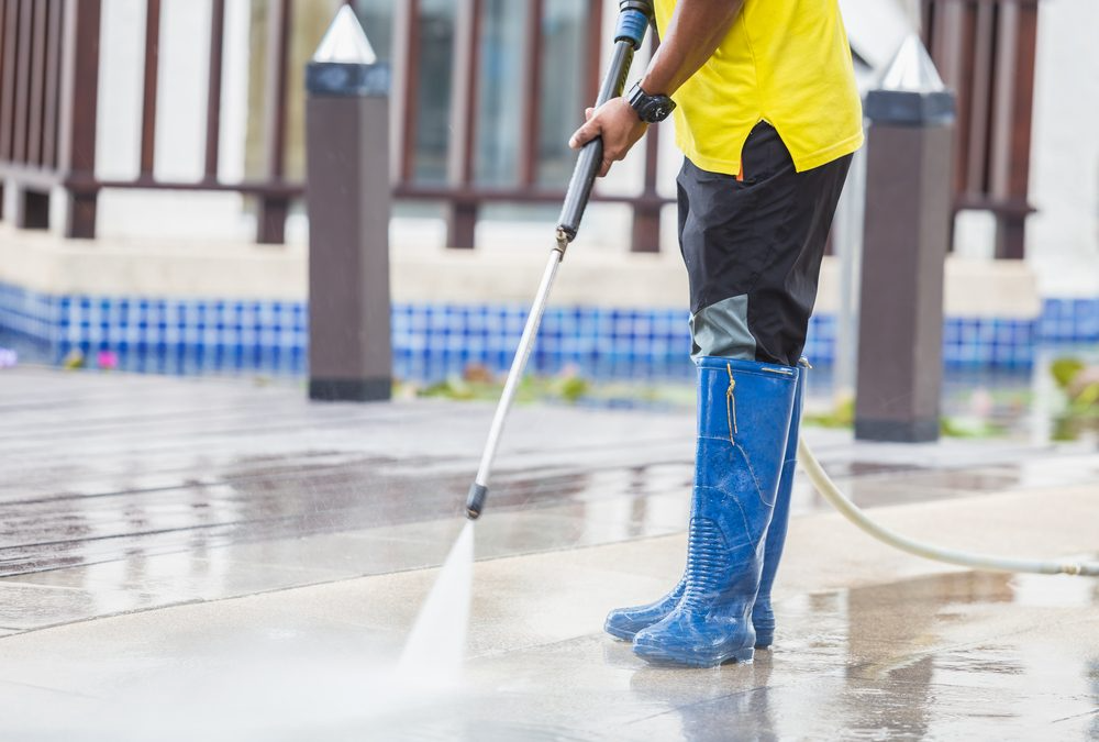 Person in blue boots power washing an outdoor surface with a pressure washer on a wet patio.