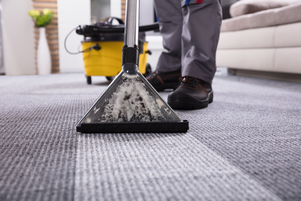 download (75) Close-up of a person cleaning a carpet with a professional steam cleaner in a living room.