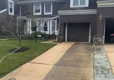 A driveway is being cleaned, showing a clear contrast between dirty and cleaned sections.